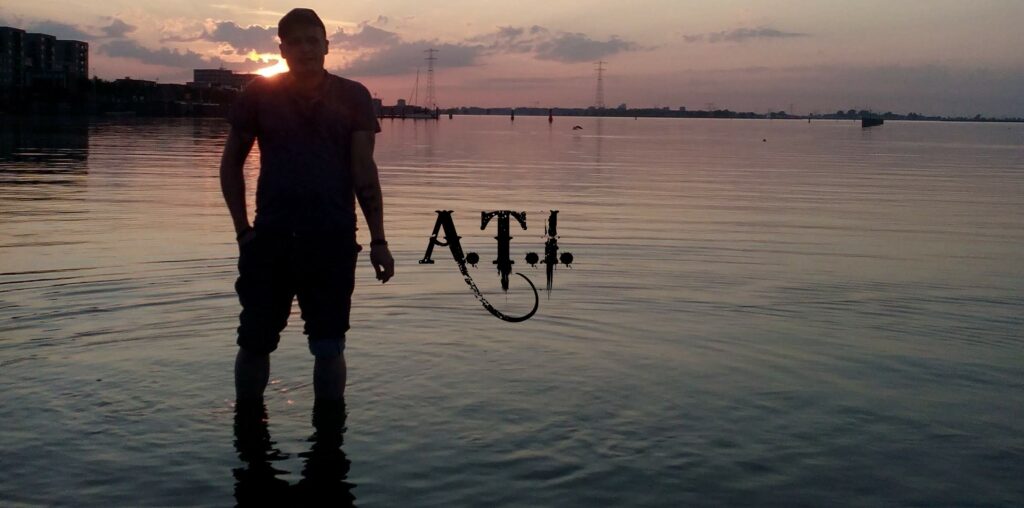 Patrik Terhorst der Band A.T.T. steht im Wasser vor einem Sonnenuntergang